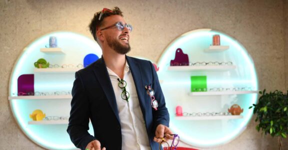 Un homme en costume marine sourit, locataire des lunettes. La boutique sur mesure est à Carcassonne.